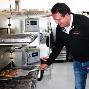 Owner of Ledgens Pizza removes a fresh baked Italian style pizza from the oven